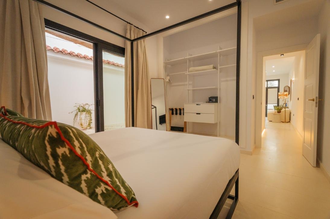 Dormitorio con cama de dosel, cojines verdes y salida al patio
